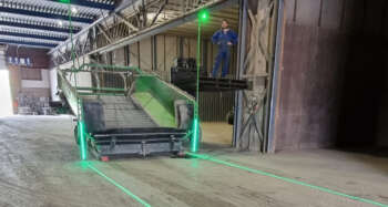 De delta fieldLAS projecteert een strakke, groene laserlijn op de vloer van een bedrijfshal voor het uitzetten van industriële vloermarkeringen.